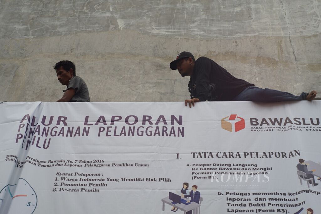 Dua pekerja memasang spanduk berisi tata cara pengaduan pelanggaran pemilu di Sumatera Utara, Senin (15/4/2019).