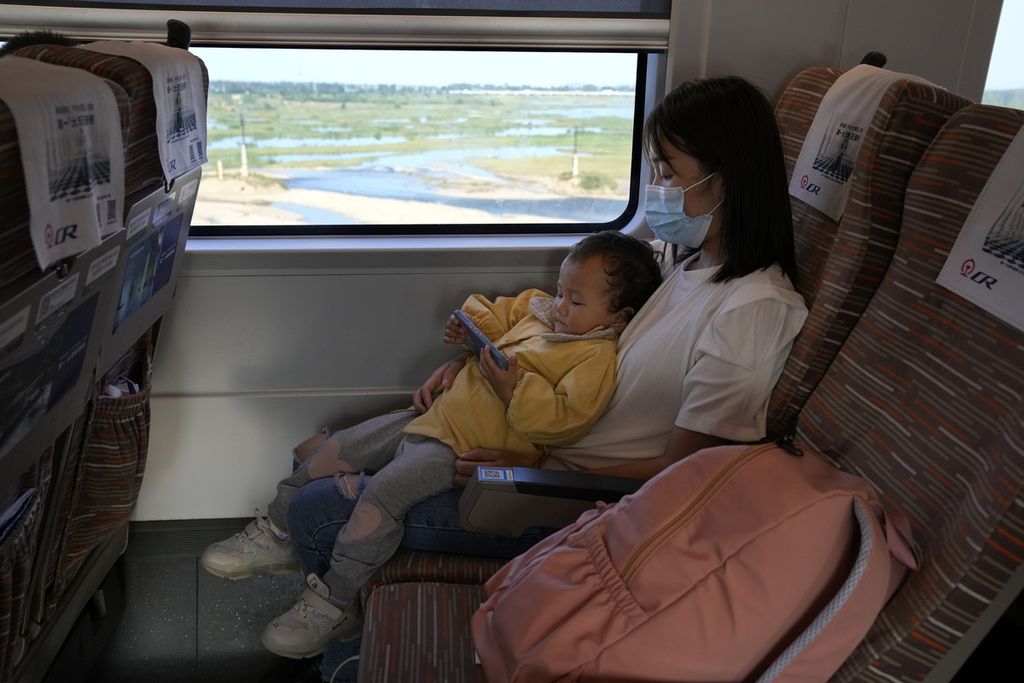 Seorang anak balita bersandar pada tubuh ibunya sambil melihat layar gawai pintar saat berada di kereta cepat dari Henan menuju Beijing, Rabu (15/9/2021). 