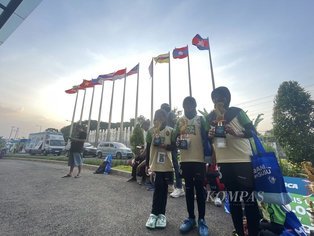 Para pesepak bola putri yunior memegang piala MilkLife Soccer Challenge 2023 edisi ketiga di depan bendera negara-negara Asia Tenggara, di halaman Supersoccer Arena, Kudus, Jawa Tengah, Minggu (17/12/2023).
