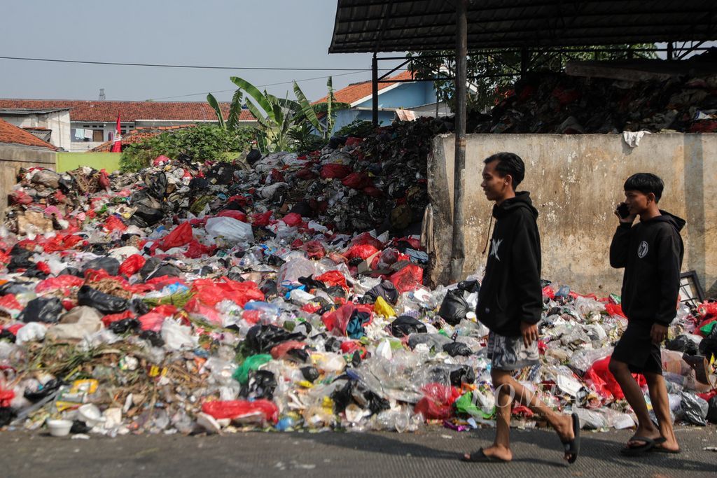 Dua remaja berjalan di samping tumpukan sampah di Jalan Naming D Bothin, Kota Depok, Jawa Barat, Jumat (28/7/2023). Tempat pembuangan sampah sementara di Jalan Naming D Bothin kelebihan sampah sehingga sampah meluber ke jalan. 