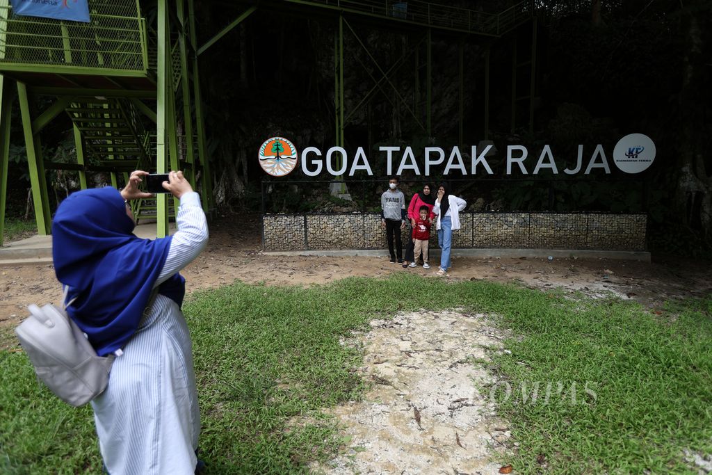 Pengunjung berfoto di depan tulisan Goa Tapak Raja di Desa Wonosari, Kecamatan Sepaku, Kabupaten Penajam Paser Utara, Kalimantan Timur, Minggu (31/12/2023).