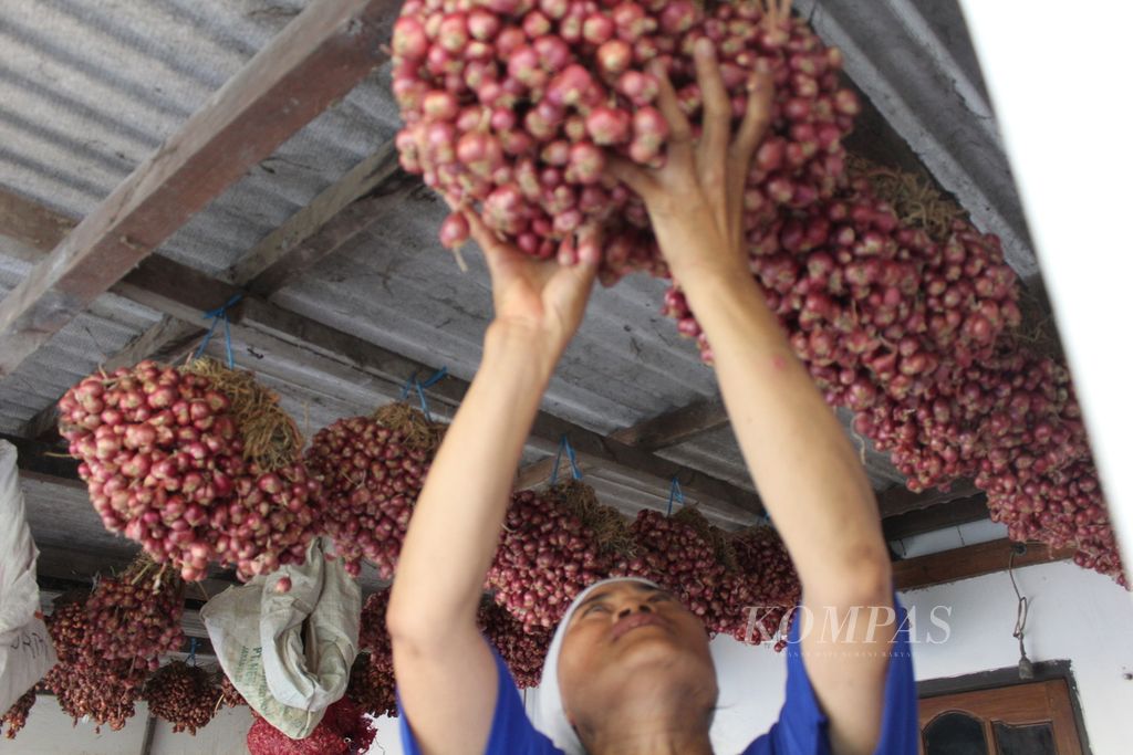 Surmi (51), perempuan buruh tani, menunjukkan hasil panen bawang merah yang digantung di rumahnya di Desa Mekarsari, Kecamatan Patrol, Kabupaten Indramayu, Jawa Barat, Kamis (12/10/2023). Bawang itu berasal dari lahan garapannya di sekitar Pembangkit Listrik Tenaga Uap Indramayu 2.