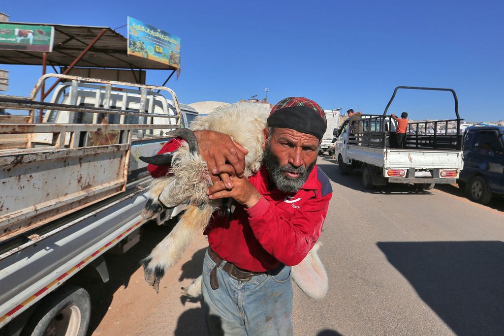 Petani Suriah menggendong kambing di pasar ternak di pinggiran kota Dana, Idlib, Suriah, Senin (4/7/2022). Di tengah konflik, perayaan kurban tetap menjadi perhatian warga setempat.