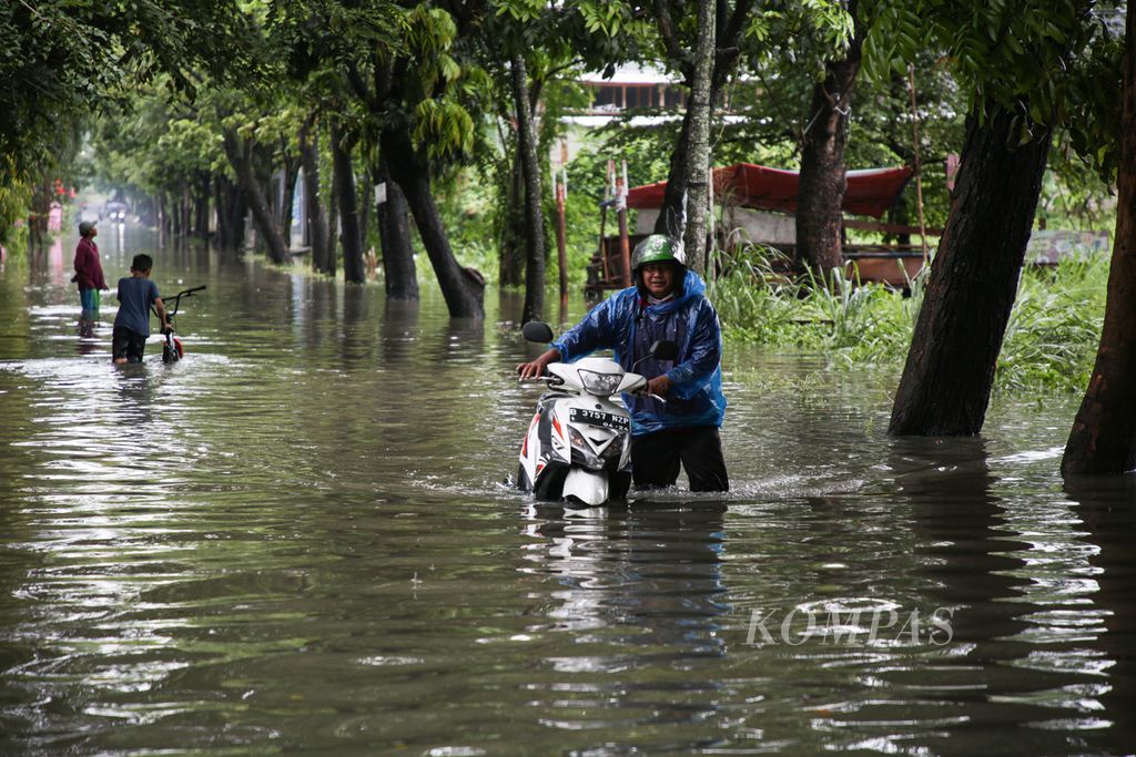Pengemudi ojek daring menuntun sepeda motornya menembus banjir di Jalan Strategi Raya, Joglo, Kembangan, Jakarta Barat, Senin (27/2/2023).