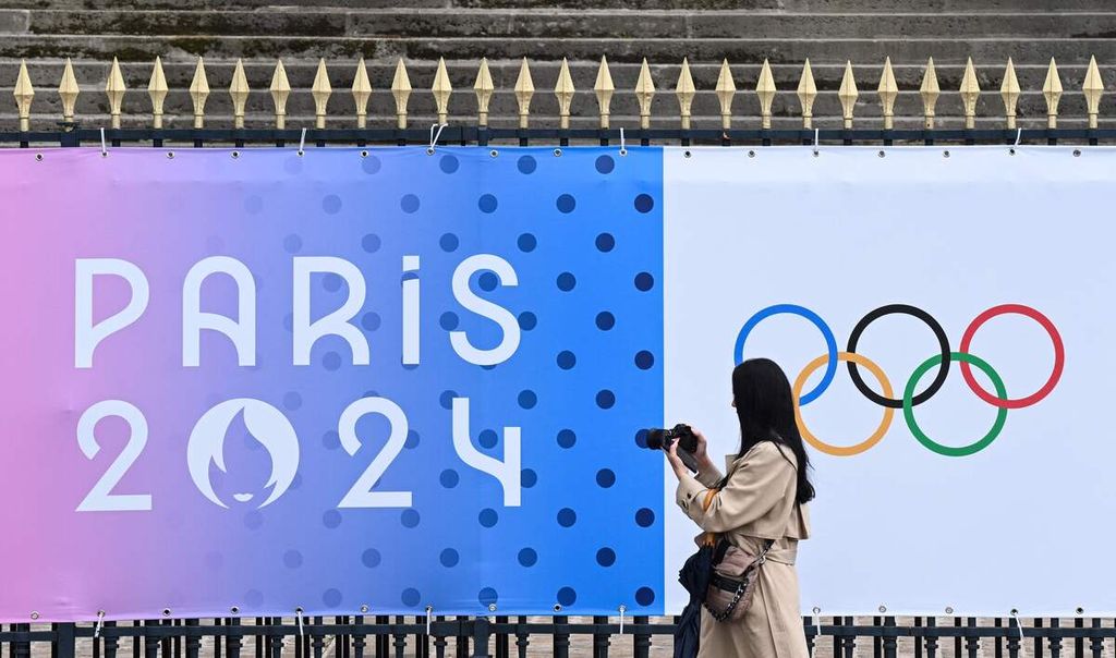 Seorang perempuan memotret spanduk bergambar logo Olimpiade Paris di luar Majelis Nasional di Paris, Perancis (5/5/2024). 