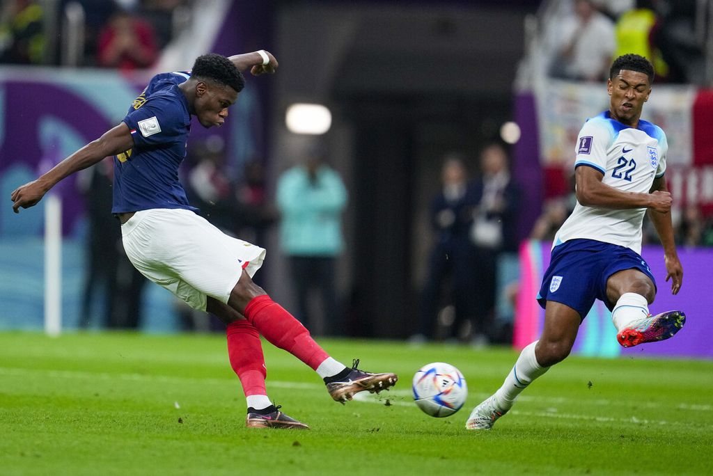Pemain Perancis, Aurelien Tchouameni (kiri), menendang bola dan mencetak gol pembuka timnya saat dikawal pemain Inggris, Jude Bellingham, pada laga perempat final Piala Dunia 2022 di Stadion Al-Bayt di Al Khor, Qatar, Sabtu (10/12/2022). Perancis menang, 2-1. 