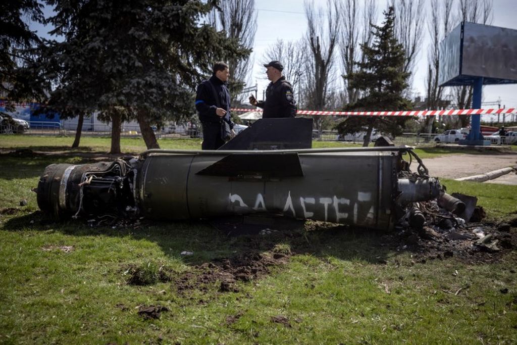 Polisi Ukraina mengamati potongan rudal besar dengan tulisan untuk anak-anak kita dalam bahasa Rusia di sebelah bangunan utama stasiun kereta api di Kramatorsk, Ukraina timur, 8 April 2022. Saat itu stasiun digunakan untuk evakuasi warga sipil. Serangan ini menewaskan sedikitnya 52  orang.