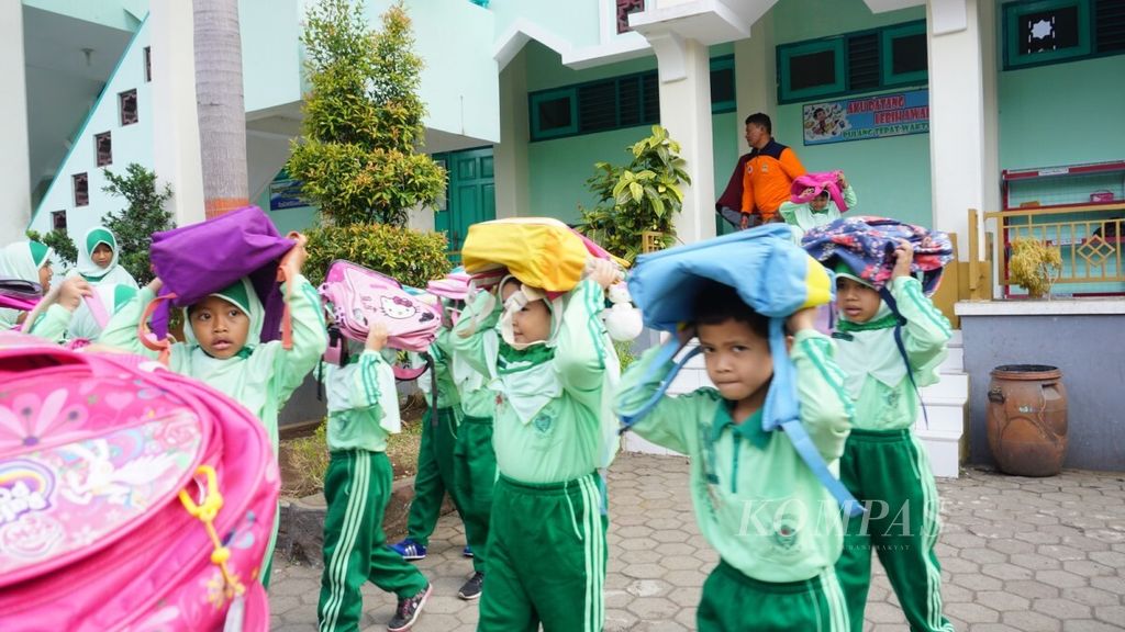 Anak-anak melindungi kepala dengan tas dalam simulasi bencana gempa bumi di Cilacap, Jawa Tengah.