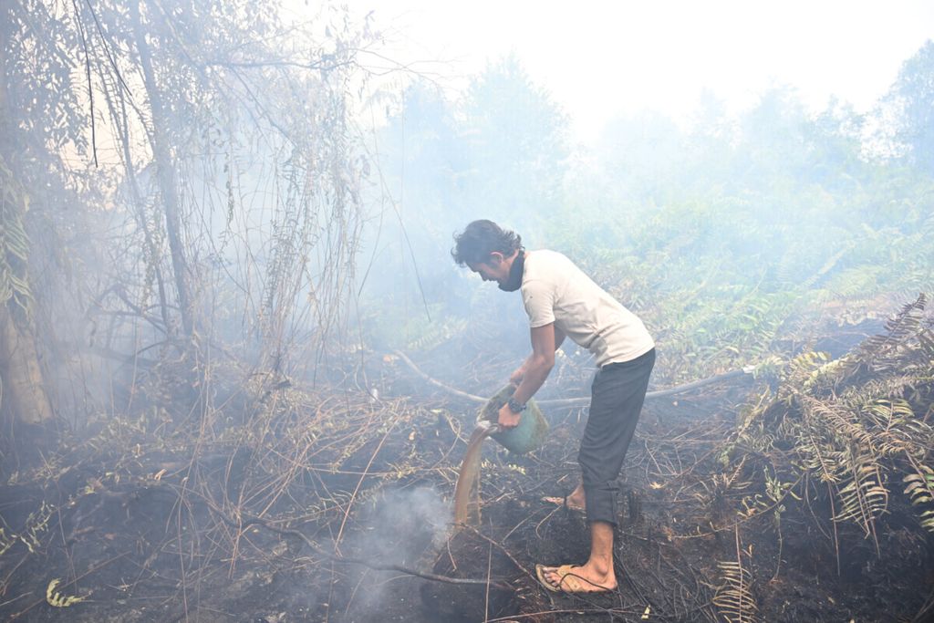 Warga menuangkan seember air ke api yang membakar lahan di belakang rumahnya di Kabupaten Kampar, Riau, Senin (16/9/2019). 