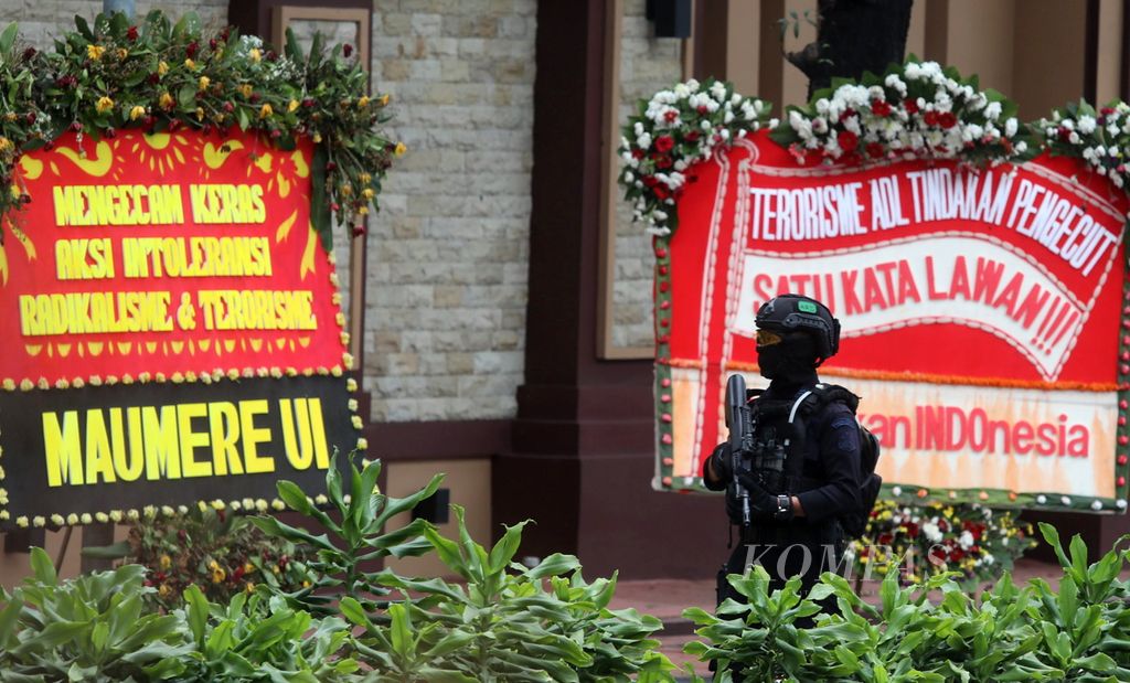 Polisi berjaga dengan senjata laras panjang di depan karangan bunga yang menyatakan dukungan terhadap pemberantasan terorisme di depan kompleks Mabes Polri, Jakarta Selatan, Kamis (1/4/2021). Polri memperketat penjagaan pasca-serangan dari terduga teroris yang tewas seusai baku tembak. 