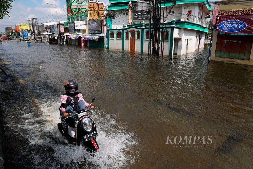 Pengemudi motor melintasi banjir dengan latar belakang kawasan pertokoan oleh-oleh yang tutup di Tanggulangin, Desa Jati Wetan, kecamatan Jati, Kabupaten Kudus, Jawa Tengah, Rabu (4/1/2023).