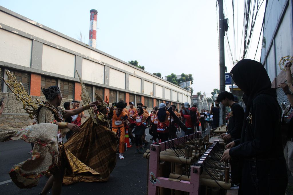 Sejumlah peserta lari berkostum (kiri) dari ajang Bank Jateng Friendship Run turut menari saat para penyemangat memainkan angklung di Jalan Cicendo, Kota Bandung, Jawa Barat, Minggu (4/6/2023).