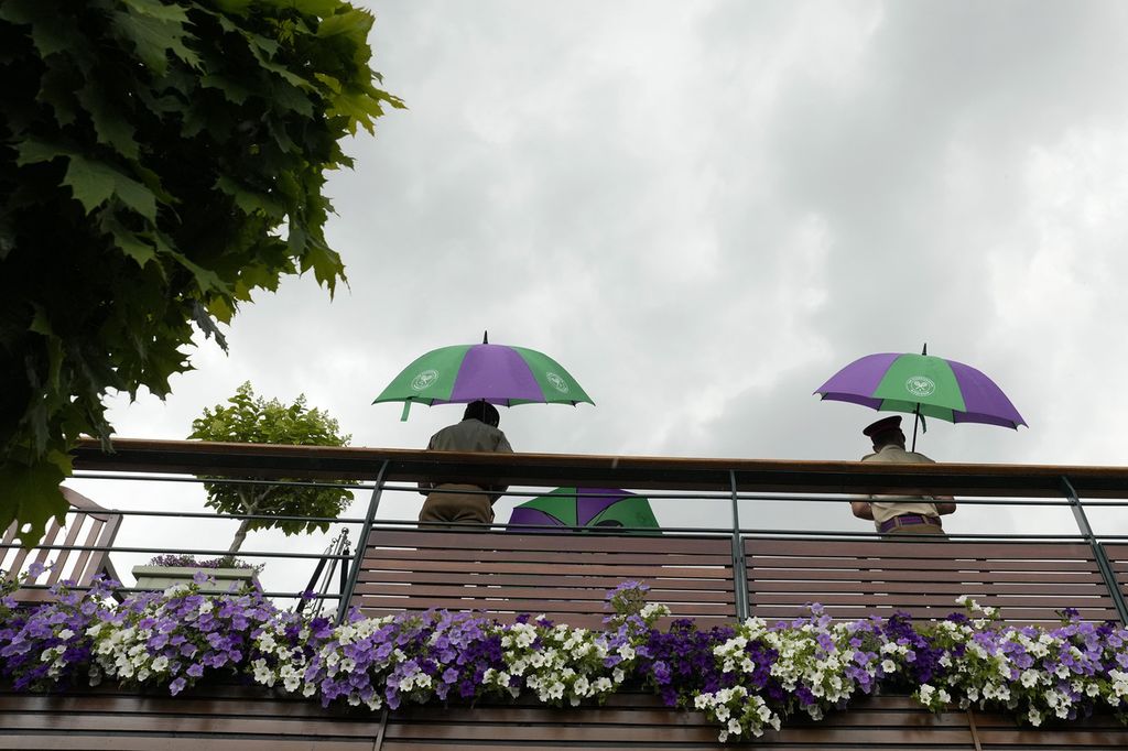 Petugas berlindung dengan payung saat hujan menunda sejumlah laga pada hari ketiga pelaksanaan turnamen tenis Grand Slam Wimbledon 2023 di All England Tennis Club di Wimbledon, Inggris, Rabu (5/7/2023).