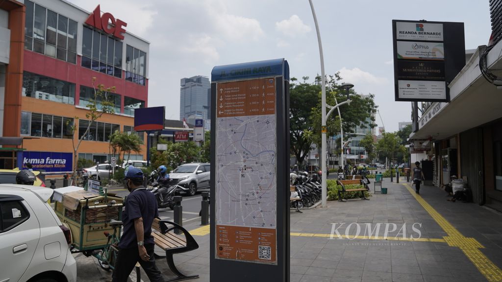 Penjual roti melintasi papan berisi informasi tempat tujuan, peta, rute, petunjuk arah dan jarak serta kode QR untuk aplikasi Jaki di Jalan Cikini, Jakarta Pusat, Selasa (8/9/2020). 