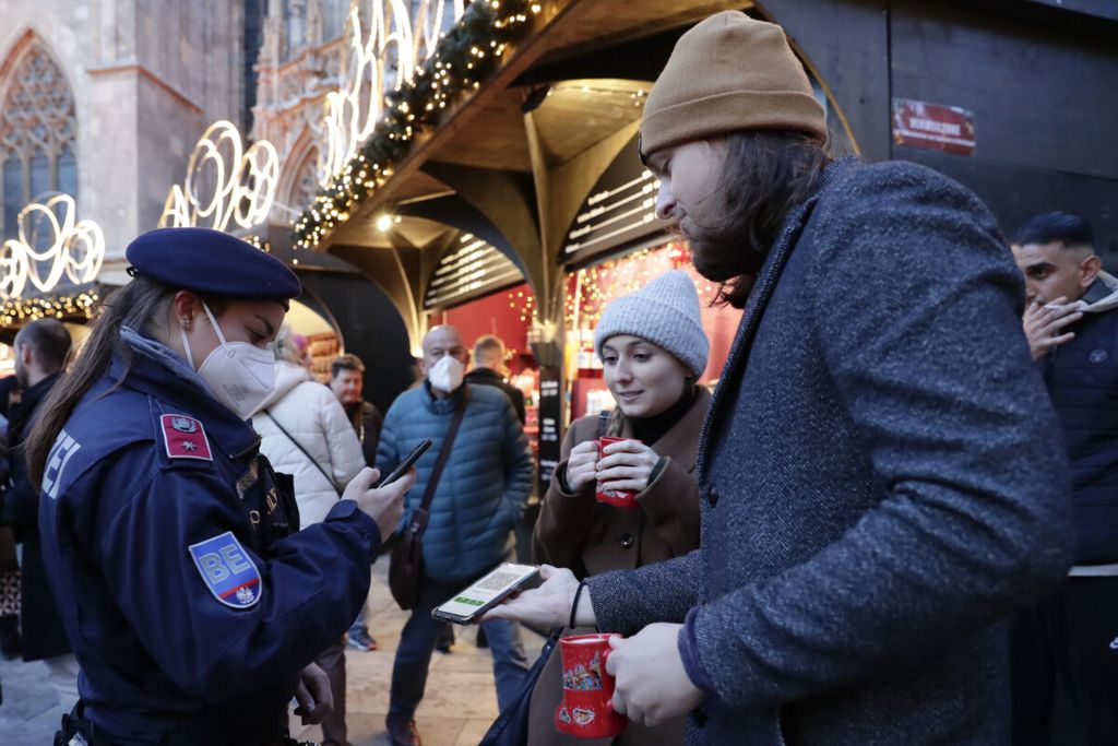 A police officer checks the vaccination status of visitors during a patrol on a Christmas market in Vienna, Austria, Friday, Nov. 19, 2021. Austrian Chancellor Alexander Schallenberg says the country will go into a national lockdown to contain a fourth wave of coronavirus cases. Schallenberg said the lockdown will start Monday, Nov.22 , and initially last for 10 days. (AP Photo/Lisa Leutner)