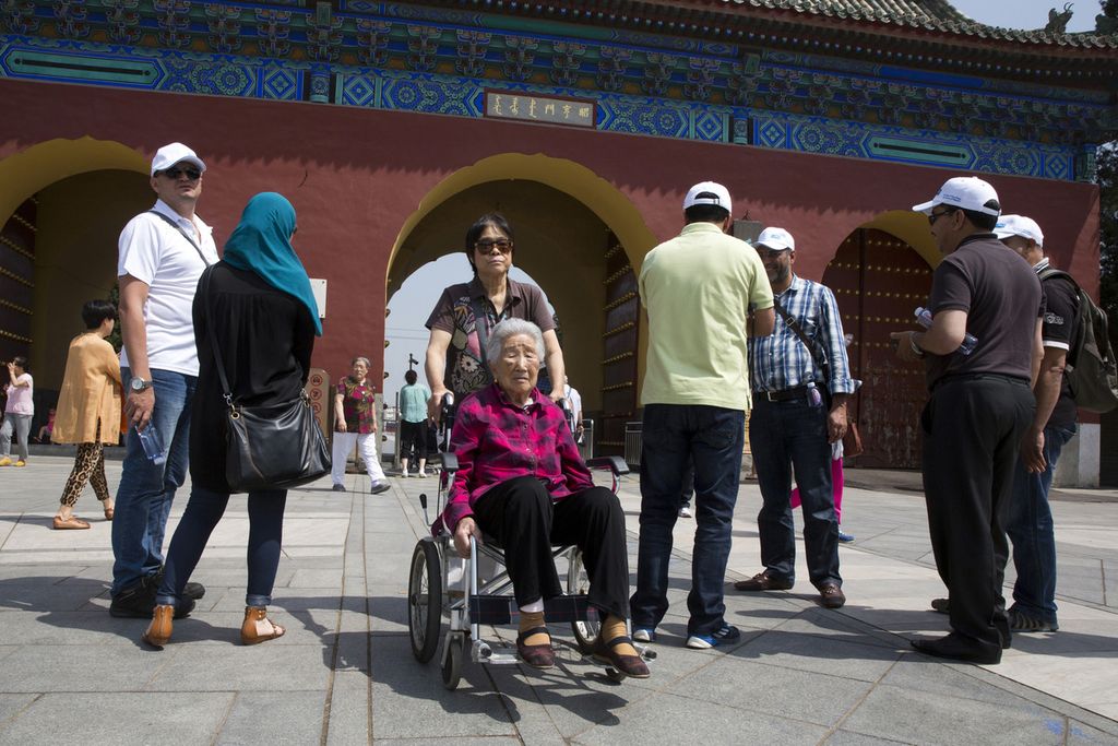 Dalam foto yang diambil pada 5 Juni 2015 ini, seorang wanita lanjut usia didorong di kursi roda dekat pintu masuk taman Kuil Surga di Beijing. 