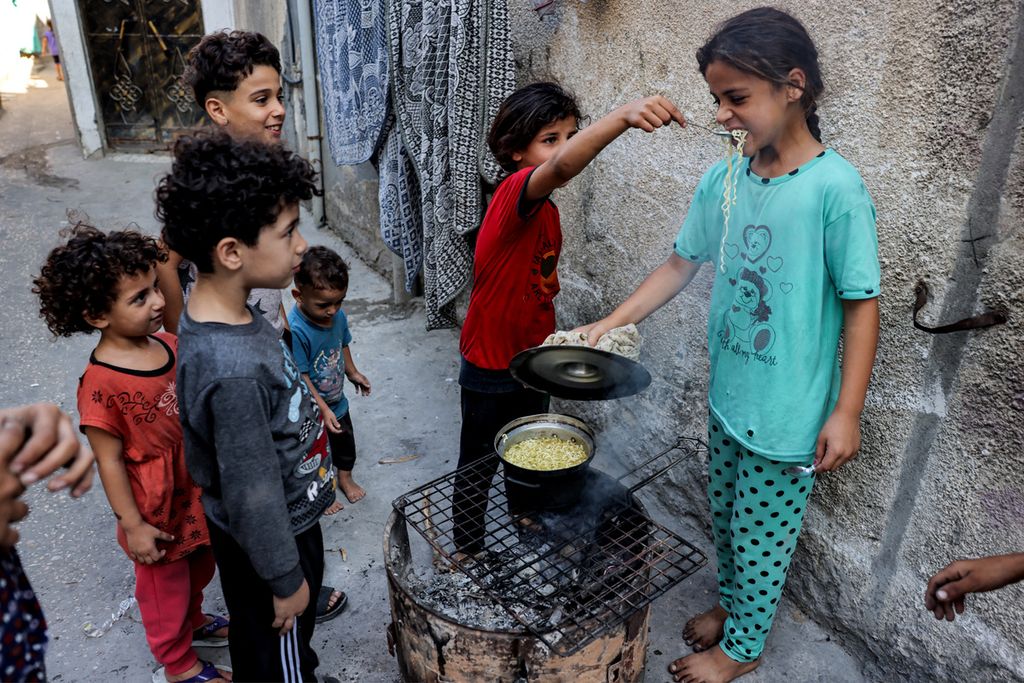 Seorang gadis memberi makan sesendok mi instan dari panci yang dimasak di atas api dalam oven darurat dari tong daur ulang, di Rafah di Jalur Gaza pada 31 Oktober 2023 di tengah pertempuran yang sedang berlangsung antara Israel dan gerakan Hamas Palestina.
