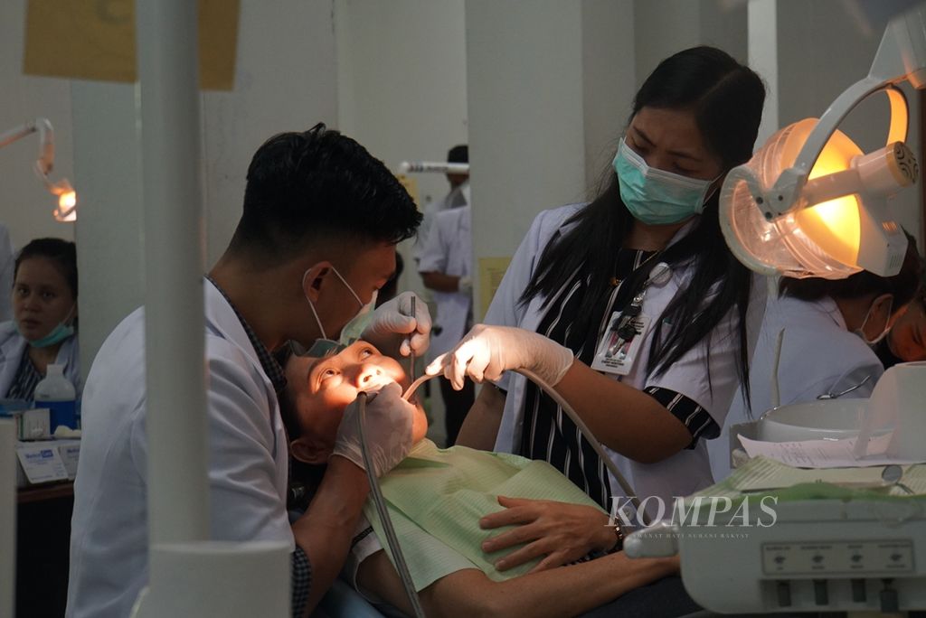 Seorang pasien menerima tindakan dari dua dokter gigi, Jumat (6/12/2019), di Rumah Sakit Gigi dan Mulut Universitas Sam Ratulangi Manado, Sulawesi Utara. 