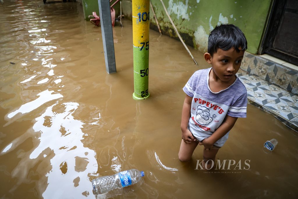 Seorang anak berdiri di samping tiang pengukur ketinggian banjir di Kampung Melayu, Jatinegara, Jakarta Timur, Jumat (1/12/2023).