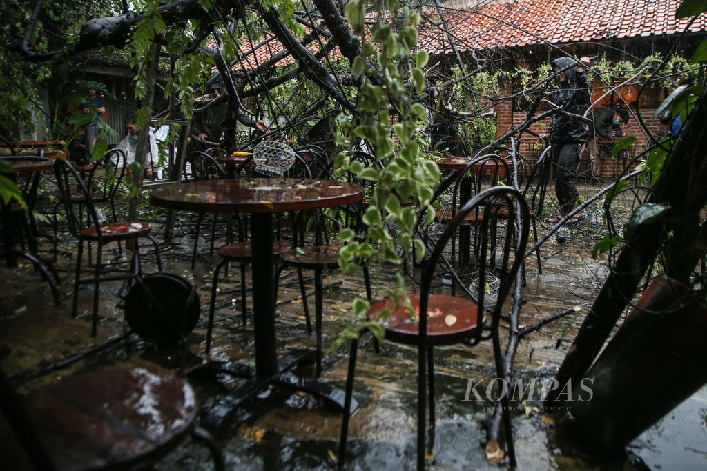 Sebuah pohon tumbang menimpa sebuah kafe saat hujan deras disertai angin melanda kawasan Cinangka, Depok, Jawa Barat, Minggu (26/9/2021). 