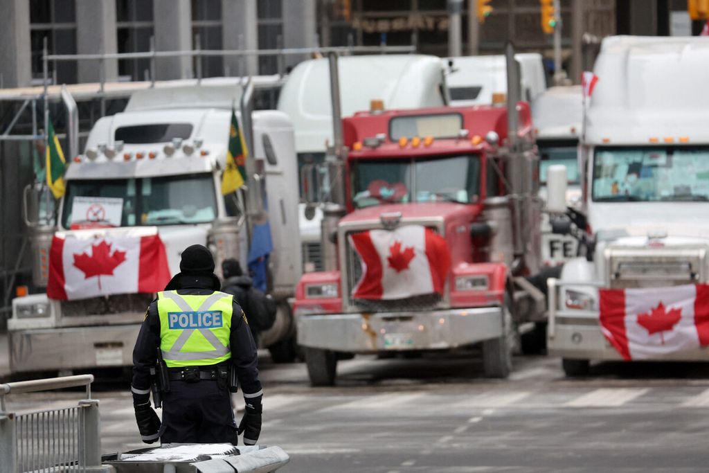 Petugas kepolisian berjaga di dekat deretan truk parkir dalam aksi demonstrasi yang dipimpin oleh pengemudi truk dengan memblokade jalan-jalan di pusat kota di dekat gedung parlemen di Ottawa, Ontario, Kanada, Rabu (16/2/2022). 