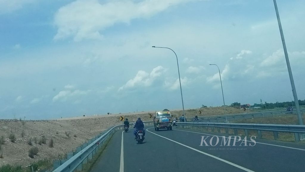 Pengendara sepeda motor melintas di jalan raya yang berada persis di luar kawasan pembangunan Bandara Dhoho (kiri) di Kabupaten Kediri, Jawa Timur, beberapa waktu lalu.