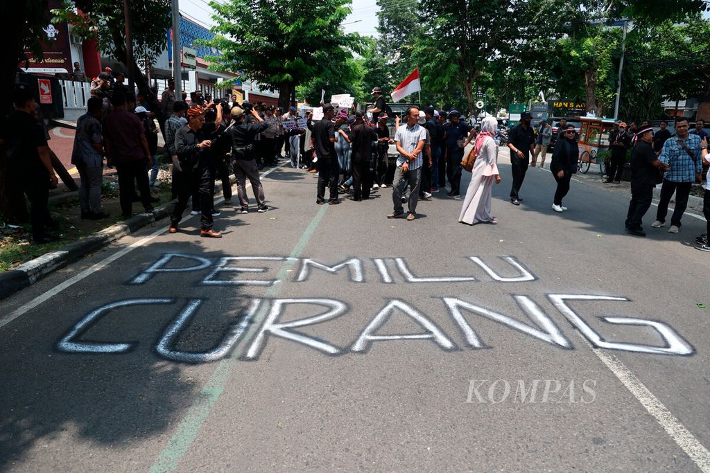 Coretan cat semprot yang bertuliskan Pemilu Curang dengan latar belakang aksi unjuk rasa di depan kantor Komisi Pemilihan Umum Jawa Tengah di Kota Semarang, Rabu (21/2/2024).
