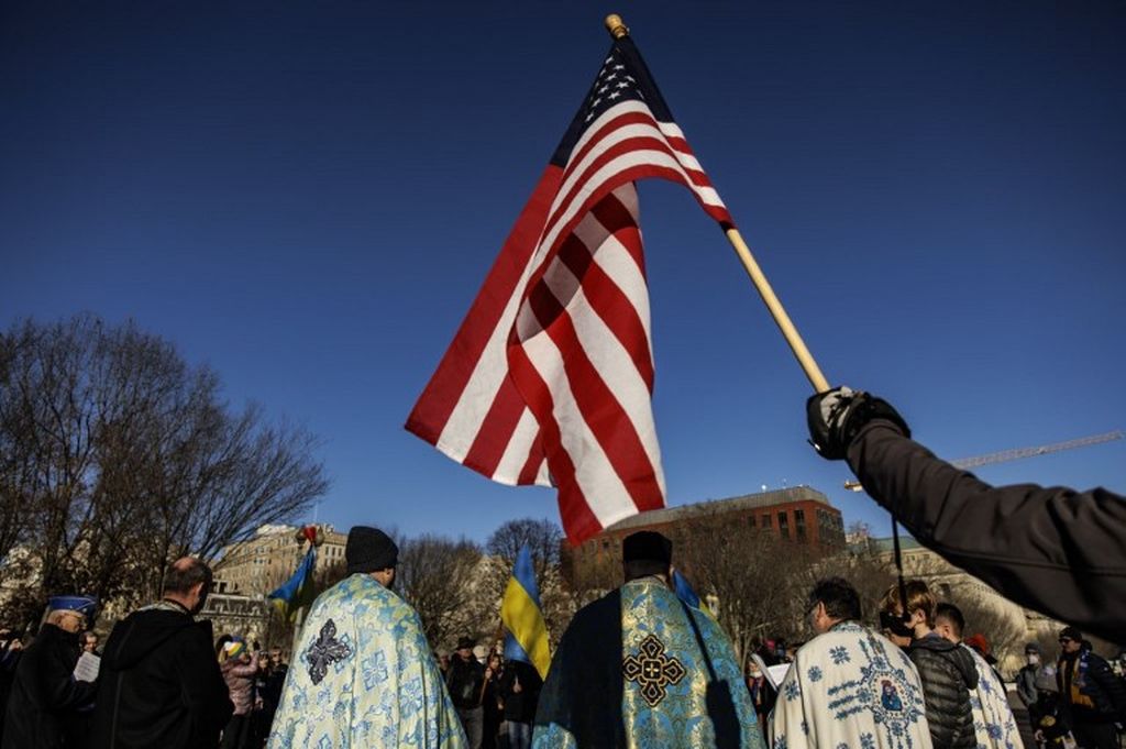 Seorang aktivis pro-Ukraina mengangkat bendera Amerika Serikat saat para aktivis berkumpul untuk berdoa dan berdemonstrasi menentang agresi Rusia di depan Gedung Putih, 6 Februari 2022, di Washington DC. Rusia telah mengumpulkan 10.000 tentara di perbatasannya dengan Ukraina dalam upaya untuk menekan Ukraina agar tidak bergabung dengan NATO. 