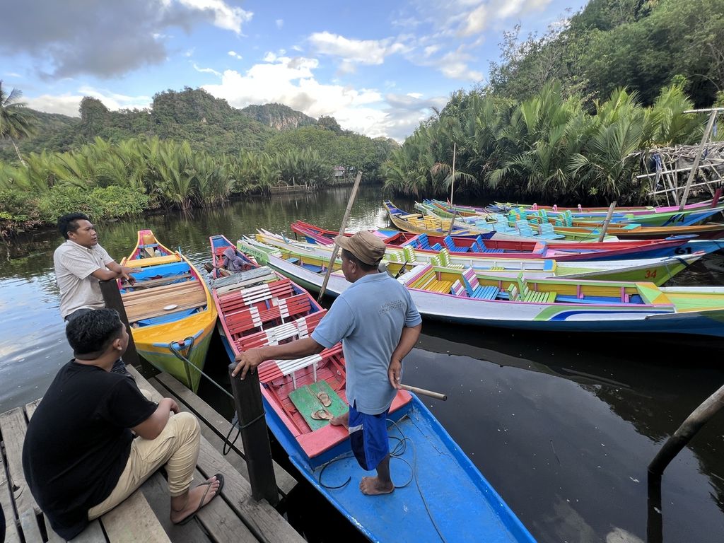  Daeng Serang (Bertopi), seorang pemilik perahu, berbincang dengan wisatawan di Dermaga 2, kawasan wisata Kampung Karst Rammang-Rammang, Maros, Sulawesi Selatan, Selasa (2/8/2022).