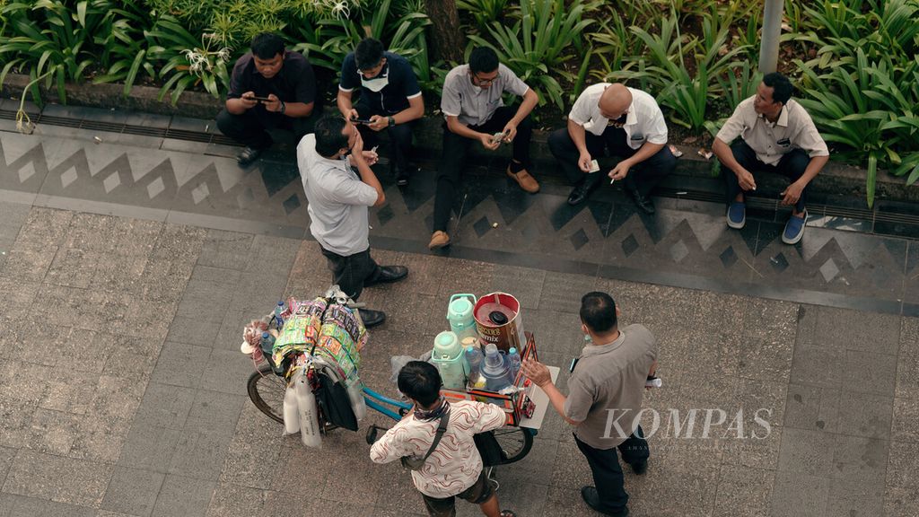 Karyawan memesan minuman kepada penjaja kopi keliling di pedestrian Jalan Sudirman, Jakarta Selatan, Senin (9/5/2022). Pemudik yang pulang kampung belum sepenuhnya mulai masuk Jakarta untuk bekerja pada hari pertama masuk kerja. 