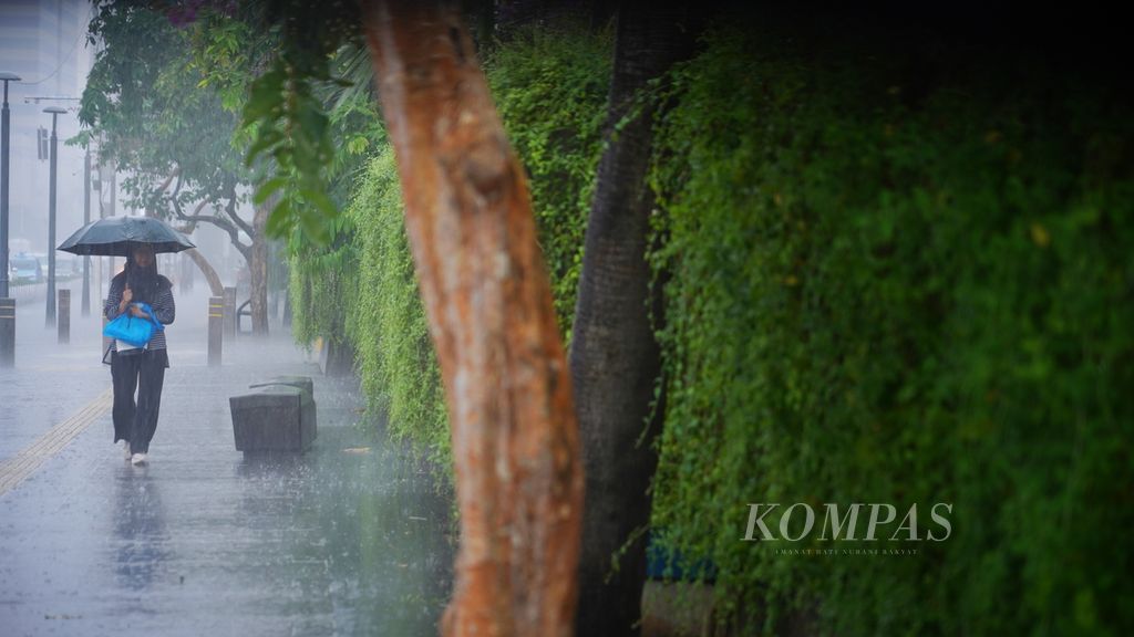 Pejalan kaki menggunakan payungnya saat melintasi trotoar Jalan MH Thamrin, Jakarta, saat hujan lebat mengguyur, Minggu (31/3/2024).  