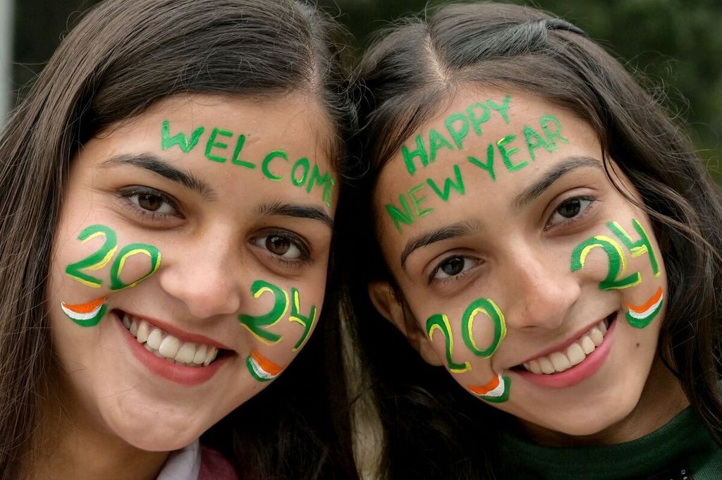 Dua perempuan berpose dengan wajah yang dilukis dengan tulisan Selamat Datang 2024 dan Selamat Tahun Baru 2024. 