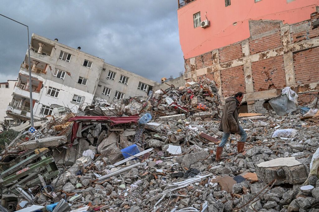 Wytekin Mumoglu, Selasa (21/2/2023), berjalan di atas reruntuhan rumahnya yang roboh akibat gempa di kota Samandag, Turki. Proses rehabiltasi dan rekonstruksi di wilayah terdampak gempa segera dimulai. 