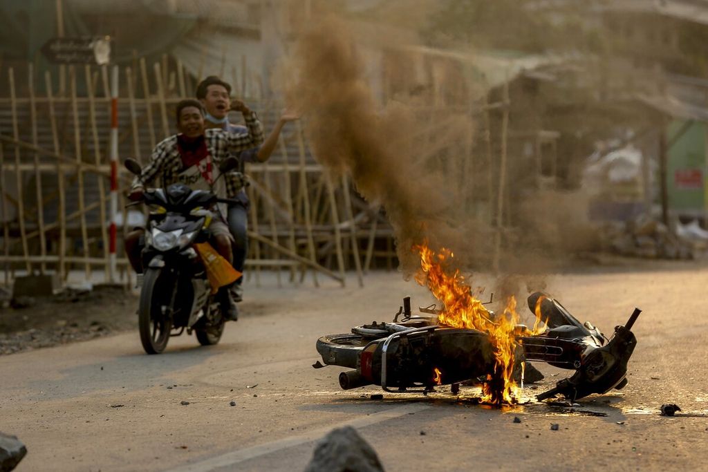 Dua pria bersepeda motor melewati sebuah sepeda motor yang dibakar saat memperingatkan warga dan pengunjuk rasa antikudeta militer ketika pasukan keamanan bersenjata tiba untuk menindak unjuk rasa di Mandalay, Myanmar, Selasa (23/3/2021). 