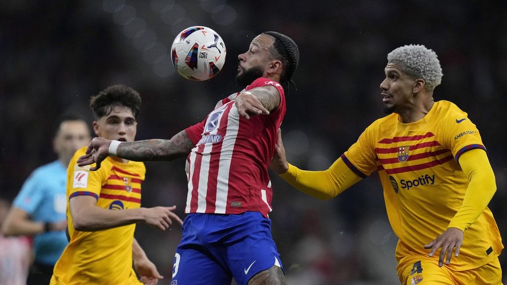 Atletico Madrid player, Memphis Depay (center), attempts to control the ball with his chest while being sandwiched by two Barcelona players, Ronald Araujo (right) and Pau Cubarsi.