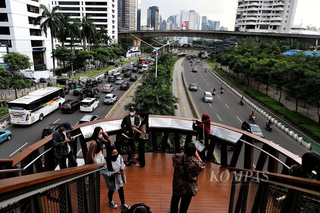 Warga menunggu waktu berbuka puasa sambil menikmati panorama kawasan gedung perkantoran dari atas jembatan penyeberangan Pinisi di Jalan Sudirman, Jakarta, April 2022. 