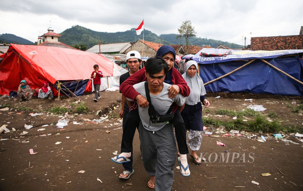 An elderly woman is carried by a man from a refugee tent to a health checkpoint in Pakuon village, Sukaresmi District, Cianjur Regency, West Java, Sunday (27/11/2022)..