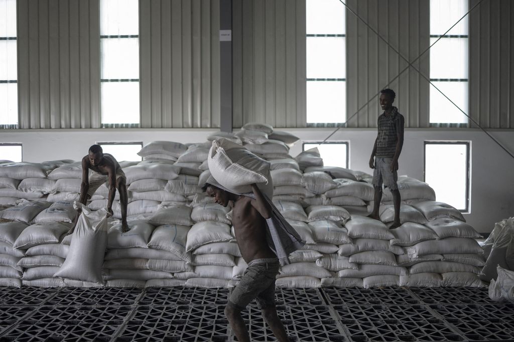 Pekerja memanggul karung berisi gandum untuk dimuat ke atas truk di gudang milik PBB di pinggiran Semera, wilayah Afar, Etiopia, Minggu (15/5/2022). Konflik di negara itu menyebabkan ratusan ribu orang di ambang kelaparan. 