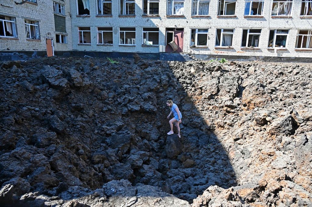 Seorang gadis tengah berdiri di dalam sebuah 'kawah' ledakan rudal Rusia yang menghantam halaman sebuah apartemen di Kharkiv, Senin (27/6/2022).