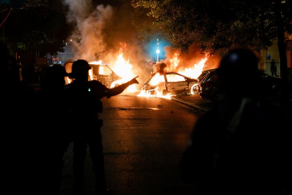 Aparat kepolisian berjaga di dekat mobil-mobil yang dibakar saat protes massa di Nanterre, sebelah barat Paris, Perancis, 28 Juni 2023. Massa memprotes kekerasan polisi yang menewaskan remaja berusia 17 tahun. 