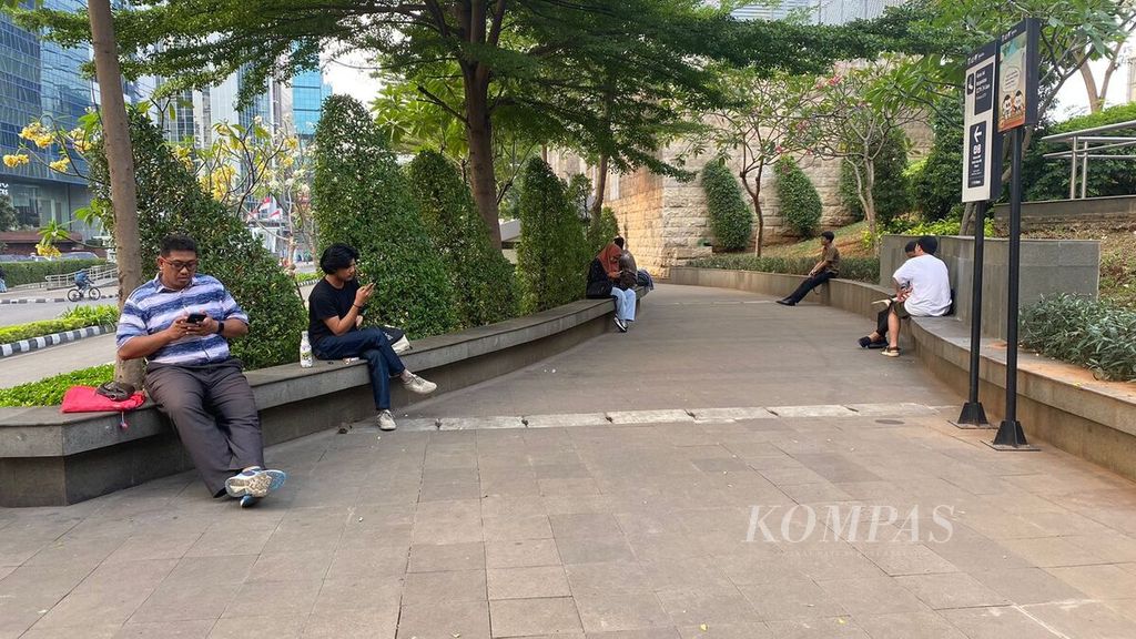 Beberapa warga duduk santai di taman di sekitar stasiun MRT Dukuh Atas, Jumat (11/8/2023).