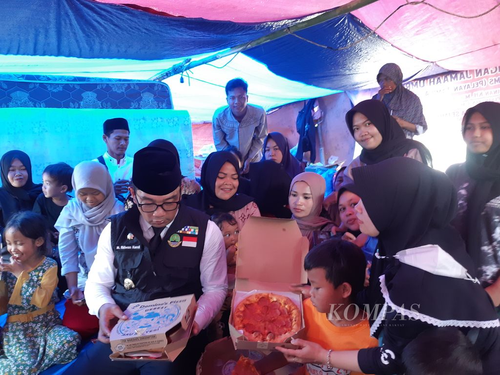 Gubernur Jawa Barat Ridwan Kamil saat mengunjungi tenda pengungsian, Kampung Gasol 2, Desa Gasol, Cugenang, Kabupaten Cianjur, Jumat (25/11/2022). Ia membagikan bahan kebutuhan pokok dan piza kepada anak-anak dan ibu-ibu.