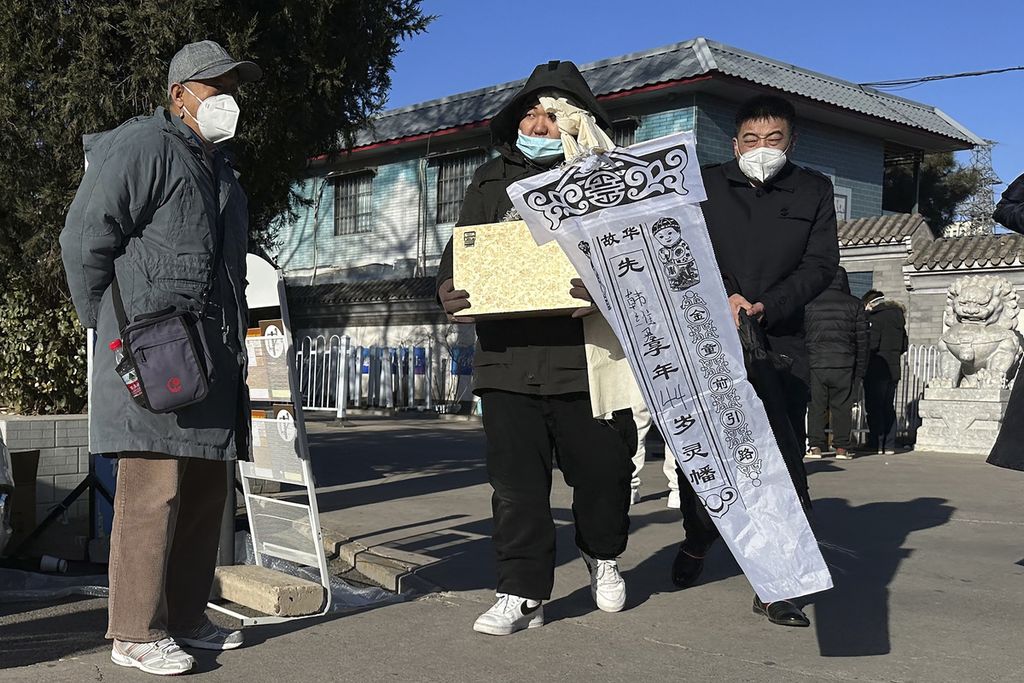 Seorang anggota keluarga membawa abu jenazah kerabatnya yang baru saja dikremasi di sebuah lokasi kremasi di Beijing, China, Sabtu (17/12/2022). Aktivitas di rumah duka dan lokasi kremasi meningkat dalam beberapa hari terakhir pasca-pelonggaran protokol kesehatan di China.