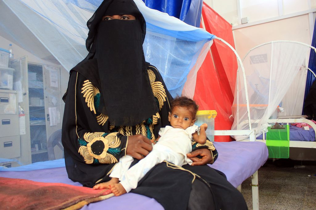 Seorang wanita duduk di tempat tidur sambil menggendong seorang anak di pusat perawatan kekurangan gizi di Provinsi Hajjah, Yaman, 22 November 2020. 