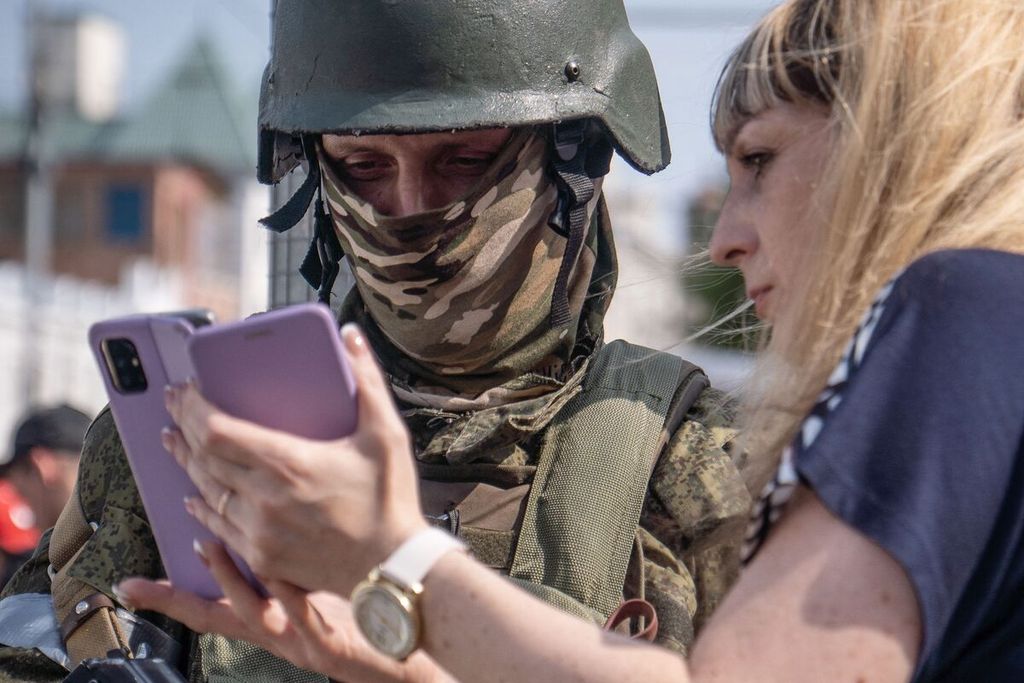 Seorang perempuan memperlihatkan telepon selulernya saat ia berbicara dengan seorang anggota pasukan tentara bayaran Wagner Group di Rostov-on-Don, Rusia, Sabtu (24/6/2023). 