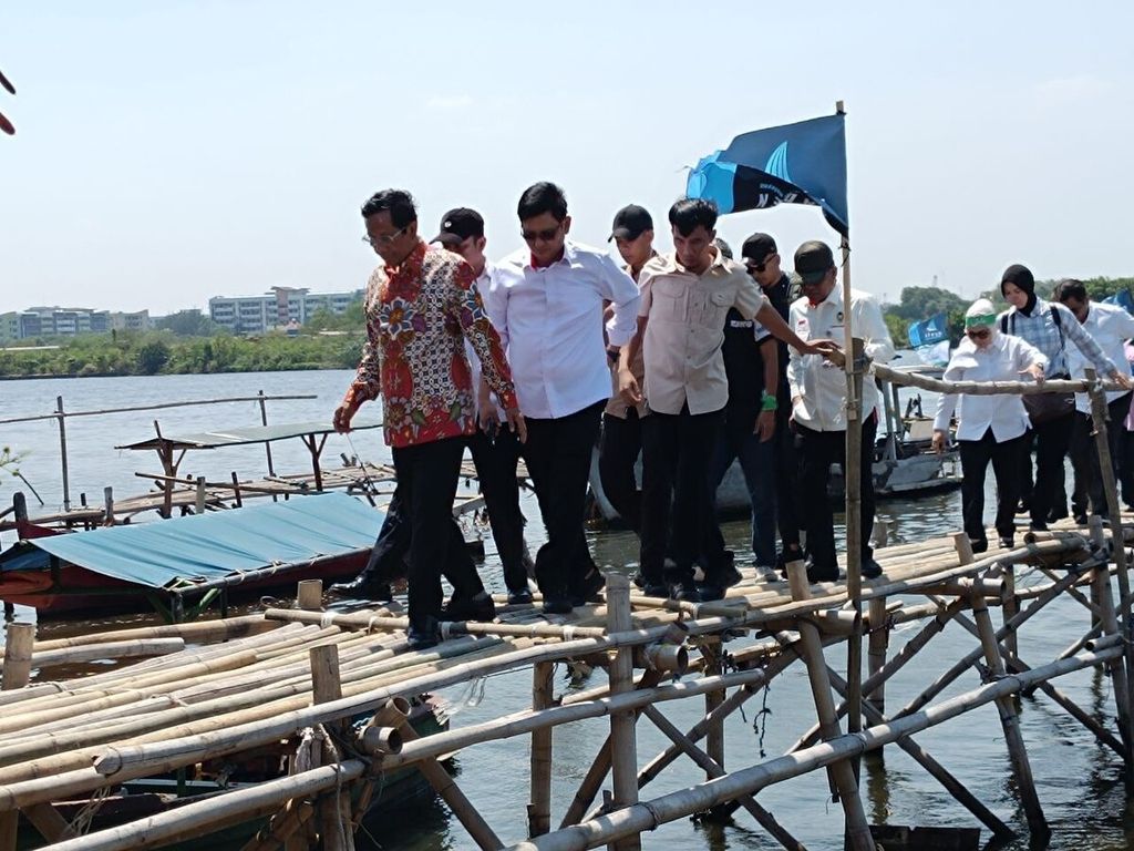 Menteri Koordinator Bidang Politik, Hukum, dan Keamanan Mahfud MD (depan) berjalan menyeberang jembatan atau dermaga bambu di kampung nelayan Marunda, Cilincing, Jakarta Utara, Rabu (20/12/2023). 