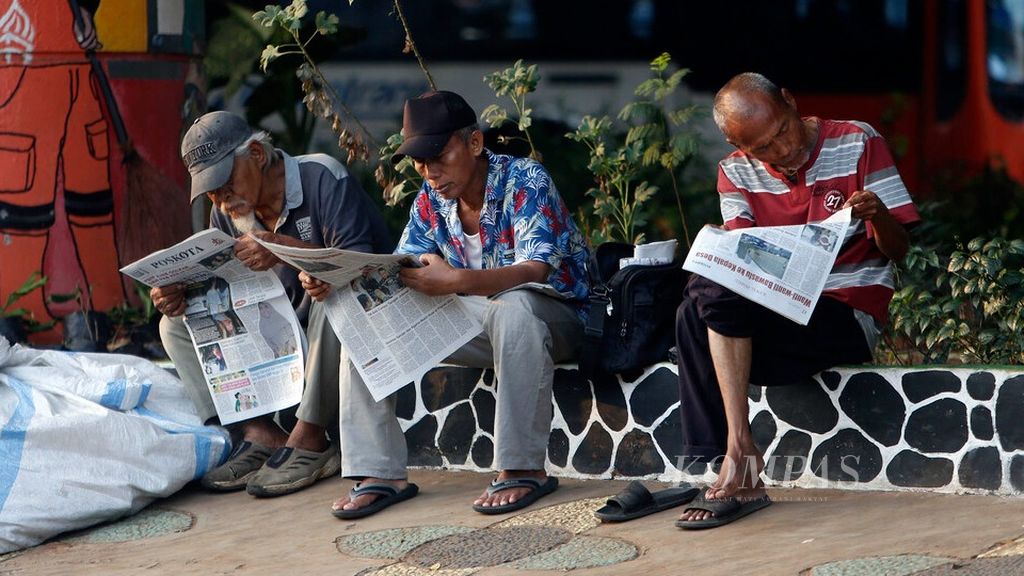 Warga berusia separuh baya menikmati paginya dengan membaca koran di bawah jalan layang Kampung Melayu, Jatinegara, Jakarta, Jumat (28/7/2023). 