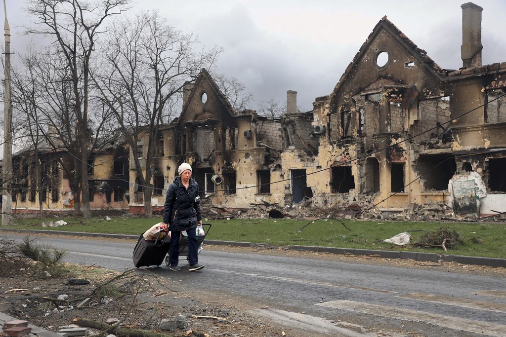 Seorang perempuan berjalan dengan menarik tasnya, melewati rumah-rumah yang hancur akibat pertempuran di Mariupol, Ukraina, 8 April 2022. 