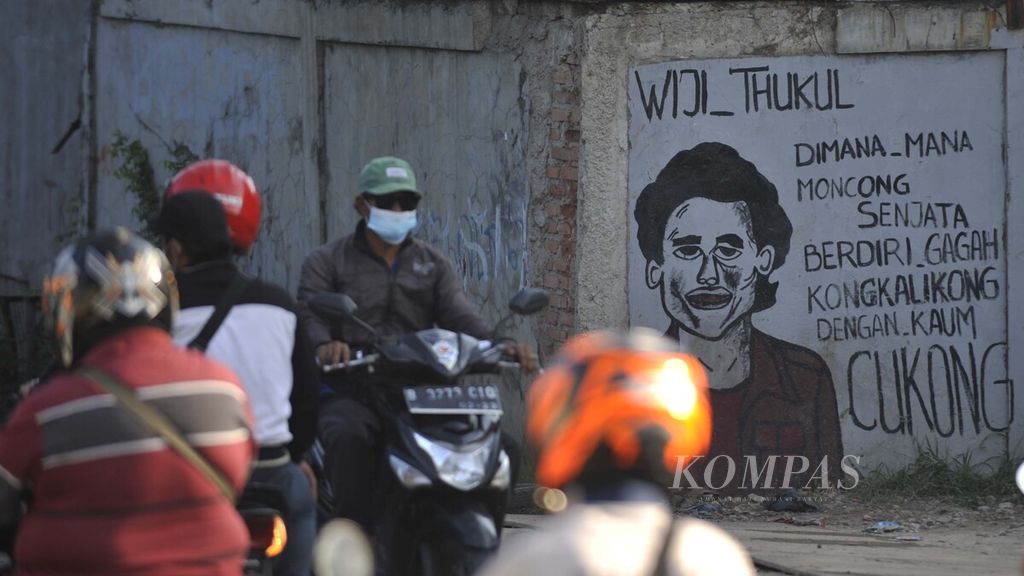 Warga melintasi mural potret penyair dan aktivis HAM Wiji Thukul di Kawasan Kota Tua, Jakarta (25/7/2020). Mural Wiji Thukul karya pelukis Bagong Surono dibuat untuk mengapresiasi semangat perlawanan Wiji Thukul terhadap penindasan rezim Orde Baru. 
