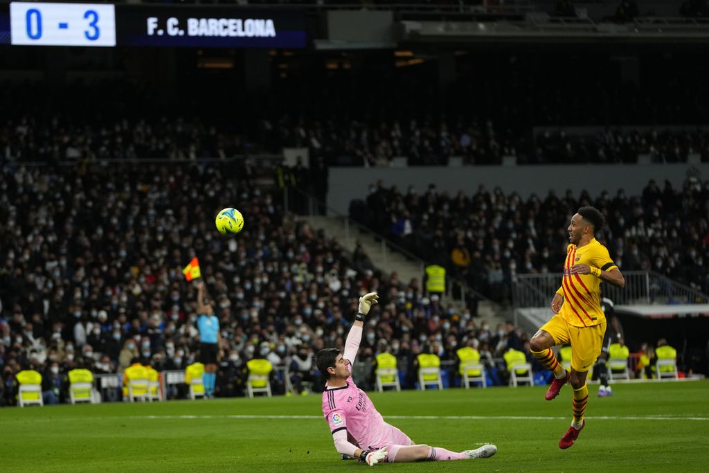 Penyerang Barcelona, Pierre-Emerick Aubameyang (kanan), menaklukkan kiper Real Madrid, Thibaut Courtois, untuk mencetak gol keduanya dalam lanjutan Liga Spanyol pekan ke-29 di Stadion Santiago Bernabeu, Madrid, Spanyol, Senin (21/3/2022) dini hari WIB. Barcelona menang 4-0 pada laga itu.